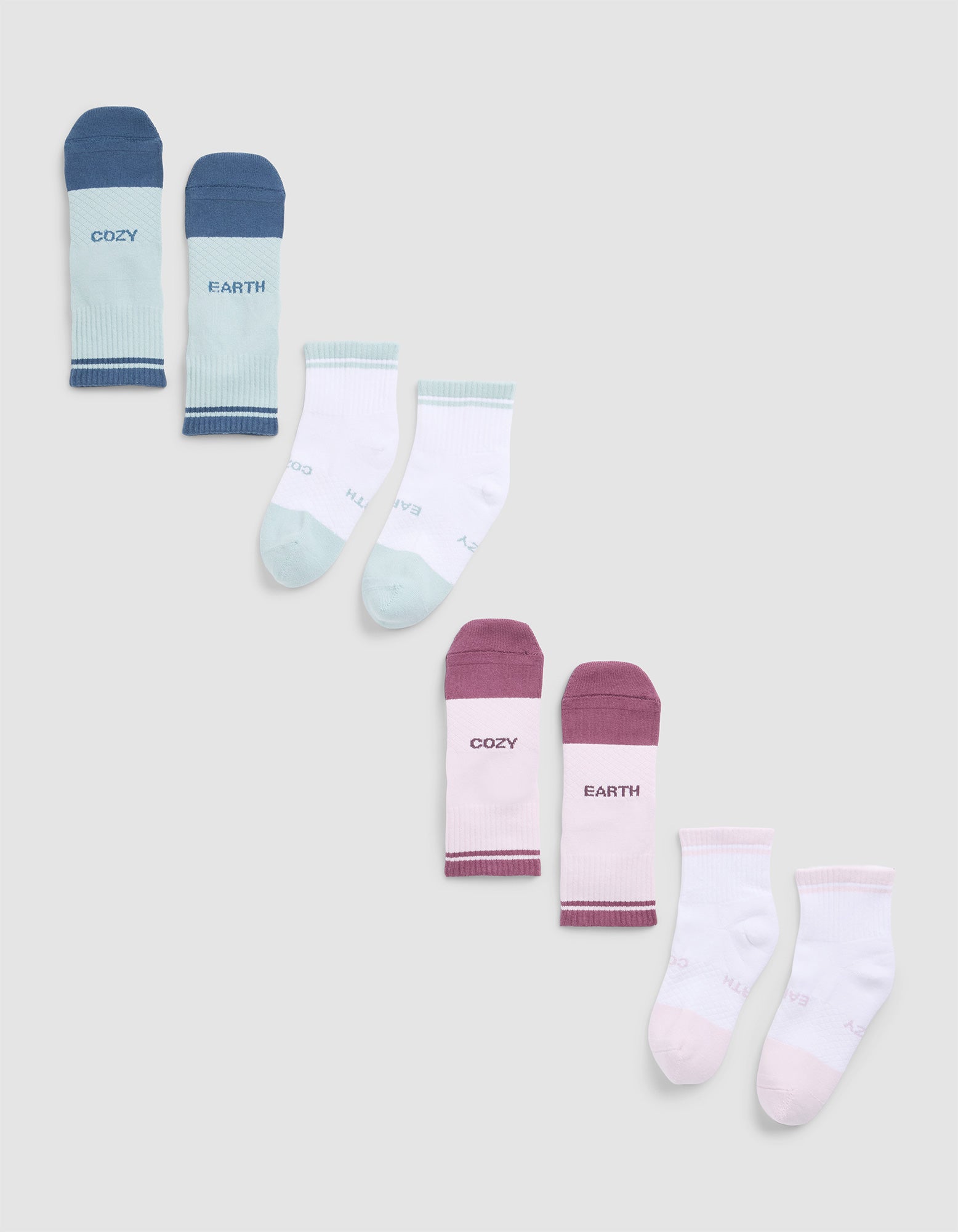 Four pairs of Essential Quarter Socks by Cozy Earth in pastel colors are displayed in a zigzag pattern on a gray background, with words like "COZY" and "EARTH" printed near the cuffs. 
