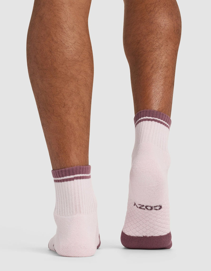 Back view of a person wearing Cozy Earth Essential Quarter Sock - Last Chance in light pink with maroon trim. The socks display the brand name on the sole as the person stands on a white background.