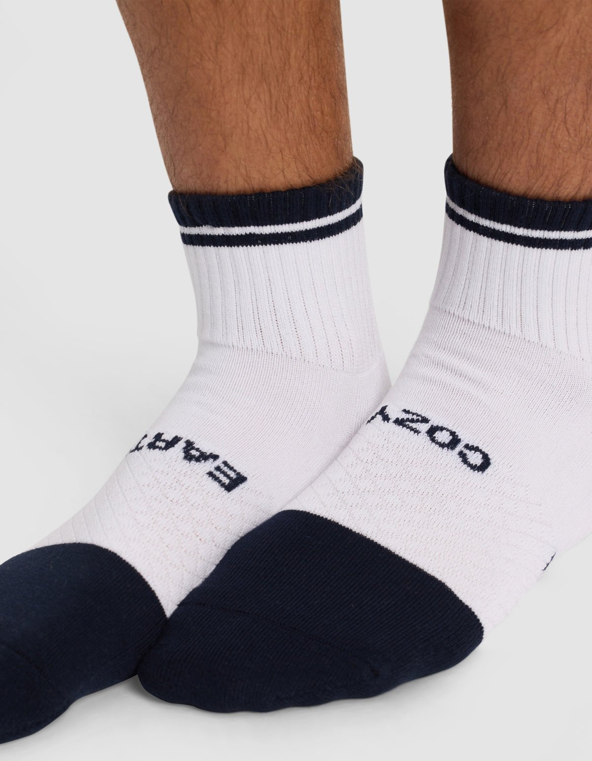 Close-up of lower legs and feet wearing Cozy Earth's Essential Quarter Sock - Last Chance, featuring white fabric, black toes, heels, and cuffs, a small black stripe near the cuff, and visible text on top.