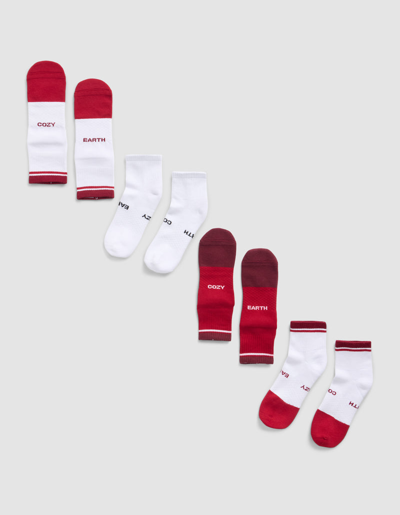 Four pairs of Cozy Earth Essential Quarter Socks are displayed diagonally on a light grey background; some feature red and white designs with “COZY EARTH” text, while others are mainly white with colored accents.