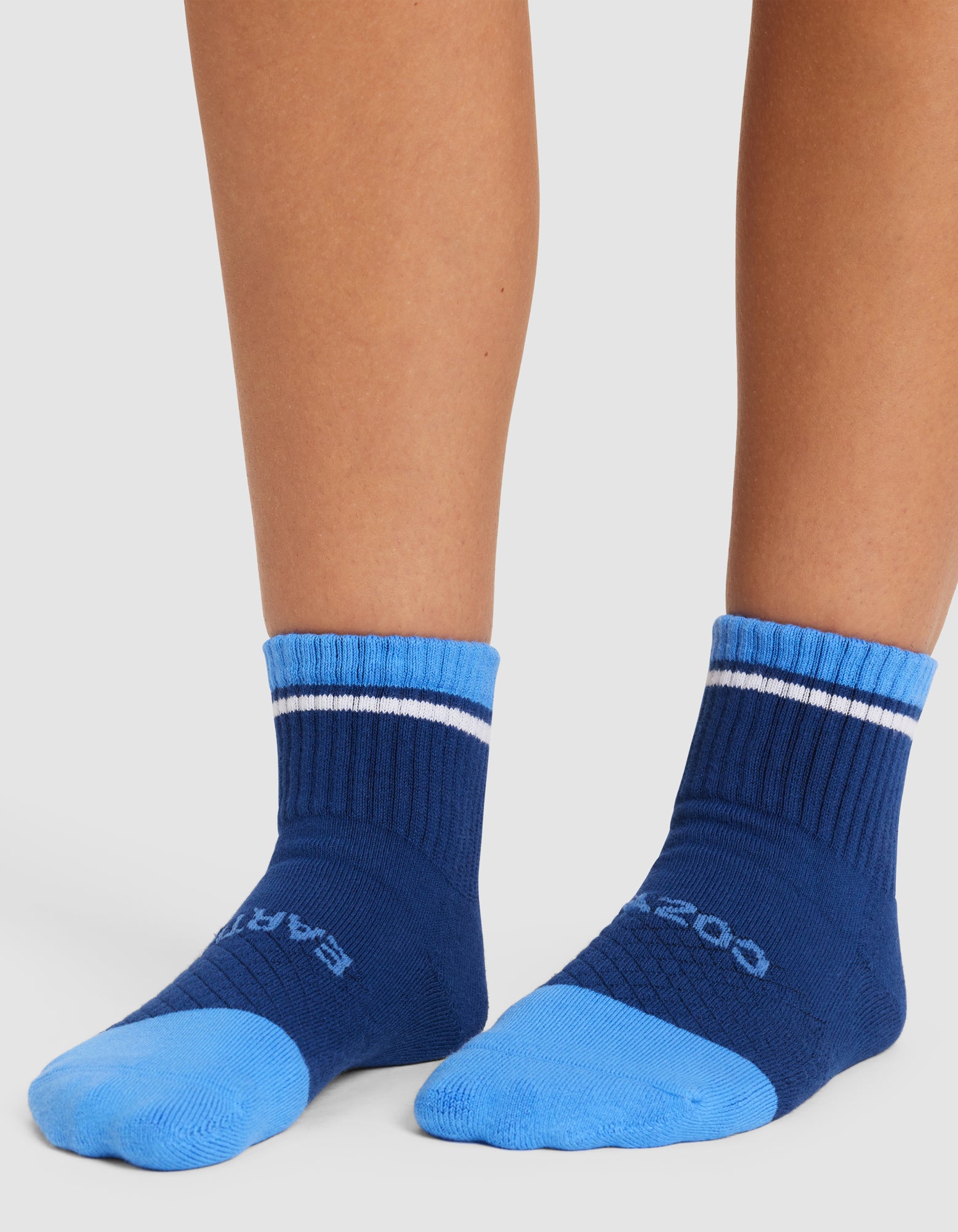 A pair of feet wearing Cozy Earth Essential Quarter Socks in blue, featuring a lighter blue toe and heel, a thin white stripe near the top, and text on the toe, set against a white background. 