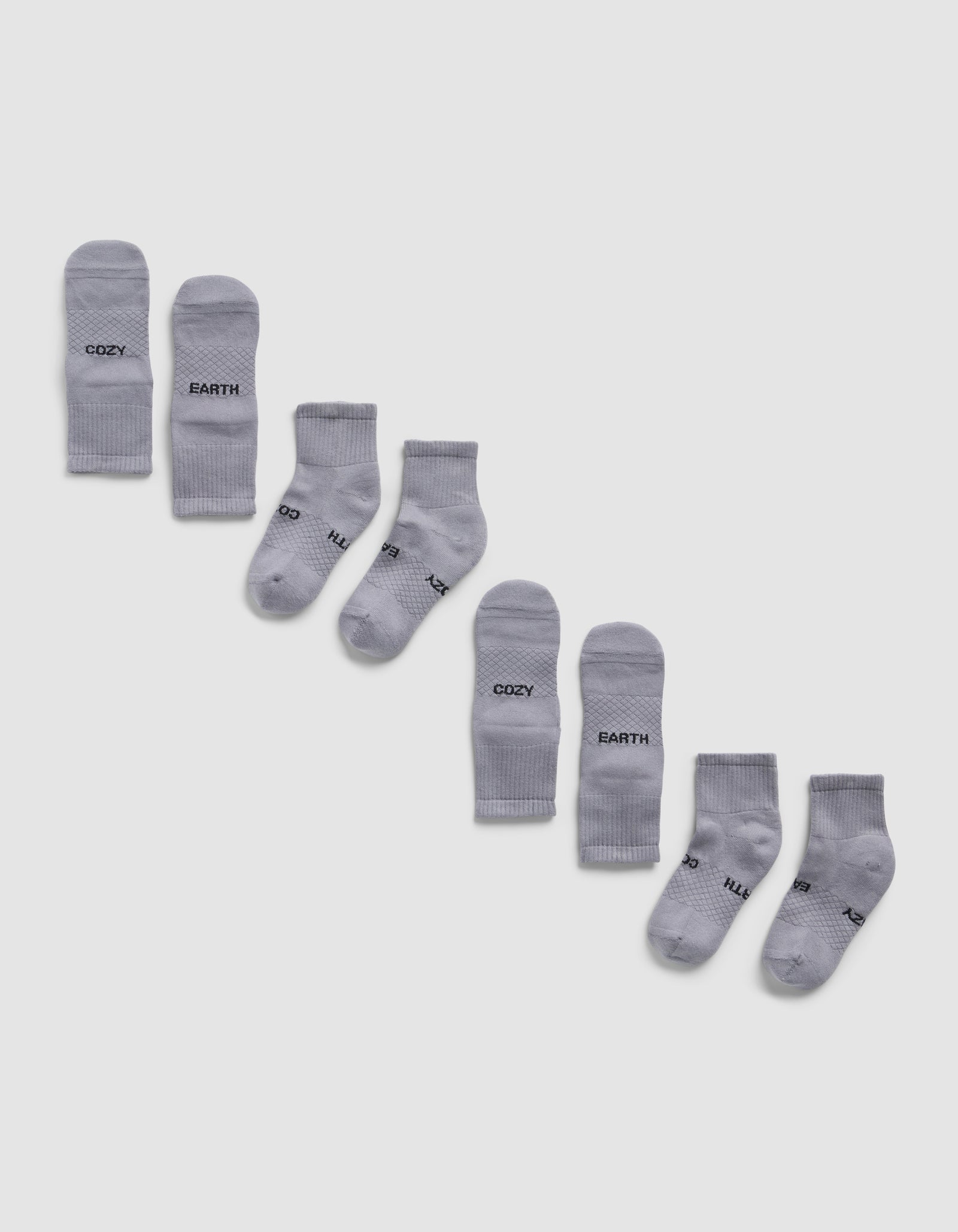 Four pairs of light gray Essential Quarter Socks by Cozy Earth are arranged diagonally on a white background, each pair featuring different words like "COZY," "EARTH," printed in black near the toes.