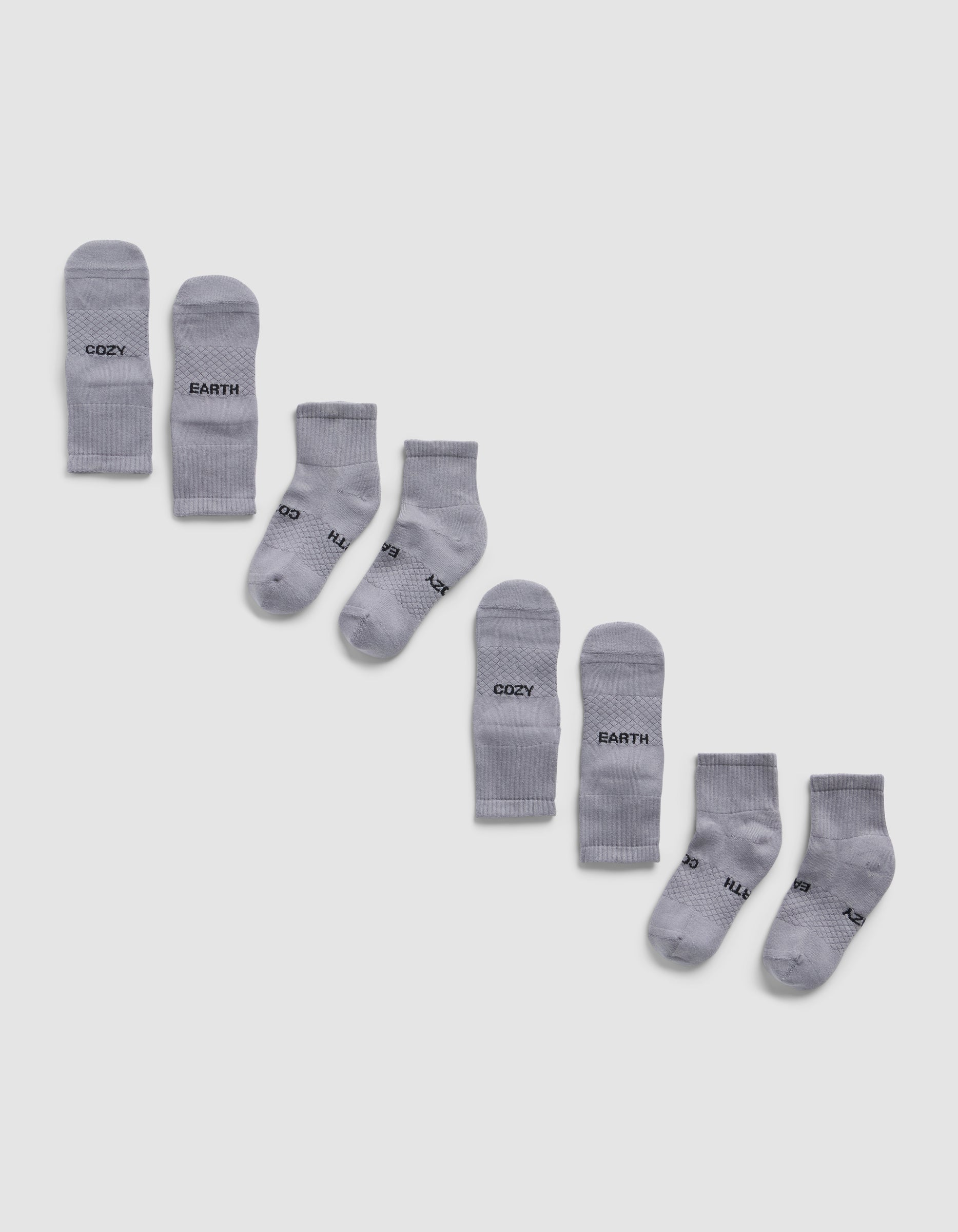 Four pairs of light gray Essential Quarter Socks by Cozy Earth are arranged diagonally on a white background, each pair featuring different words like "COZY," "EARTH," printed in black near the toes.