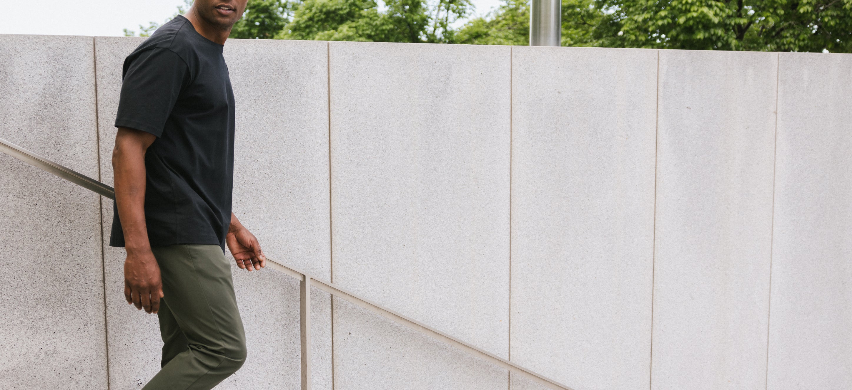 Man leaning against a light-colored wall with greenery in the background