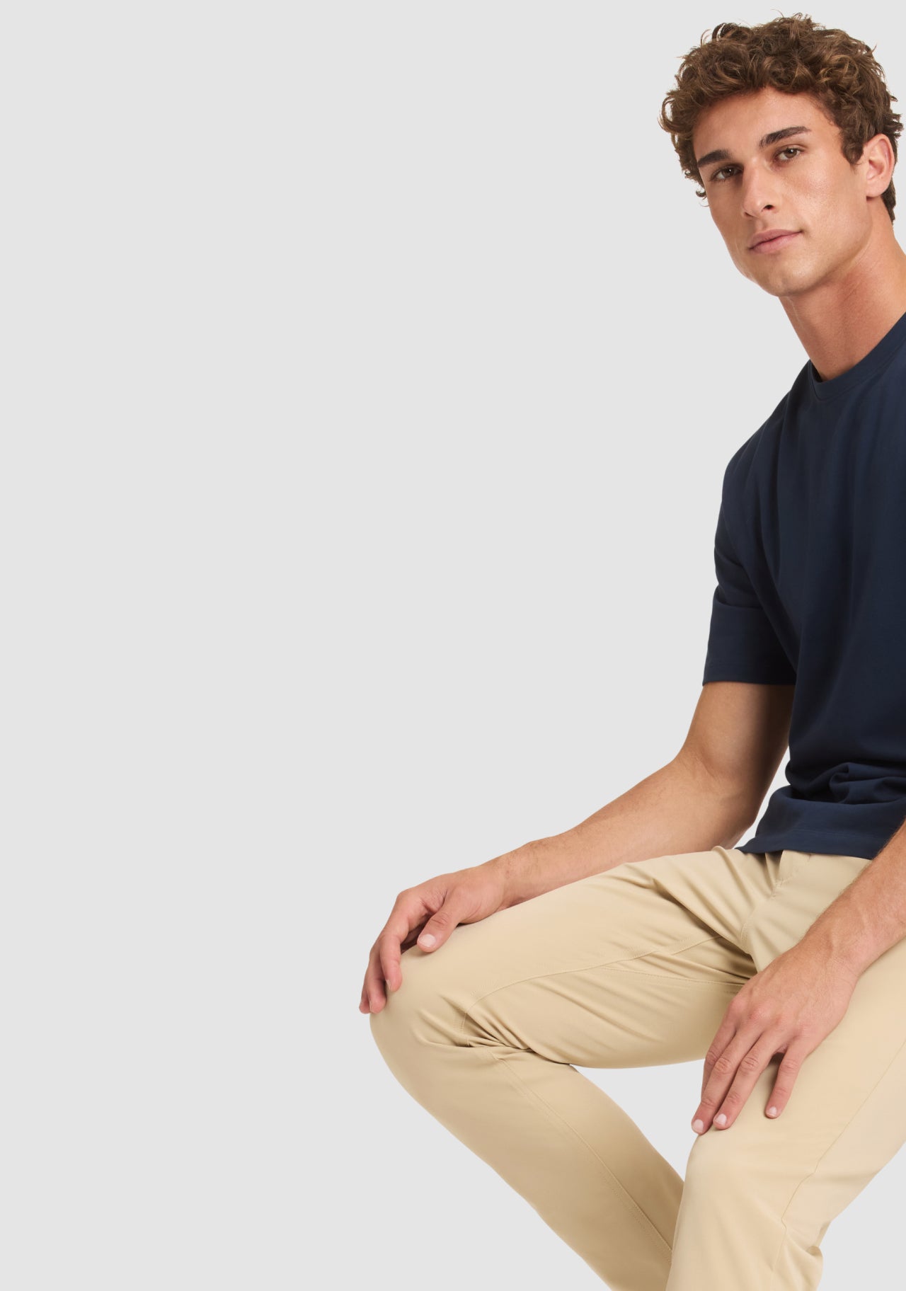 Man wearing a navy shirt and beige pants sitting on a white background