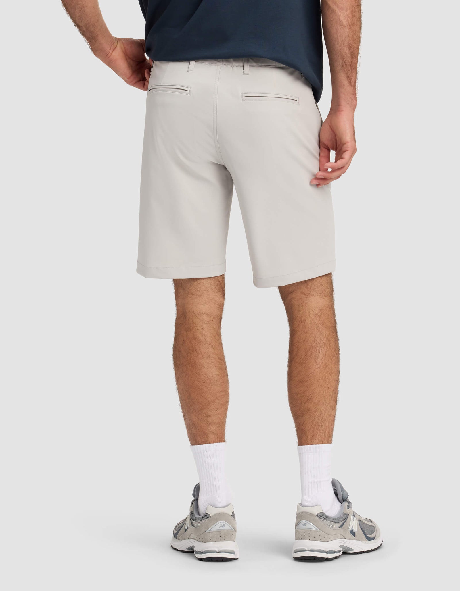 A person is shown from the back wearing Cozy Earth Men's Everywhere Shorts in light gray, paired with a dark shirt, white crew socks, and gray athletic shoes against a plain light background.