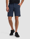 A person wearing Cozy Earth's Men's Everywhere Short in navy, a black shirt, and black athletic shoes stands with one hand in their pocket against a plain light background. Only the lower half of their body is visible.|Color:Eclipse