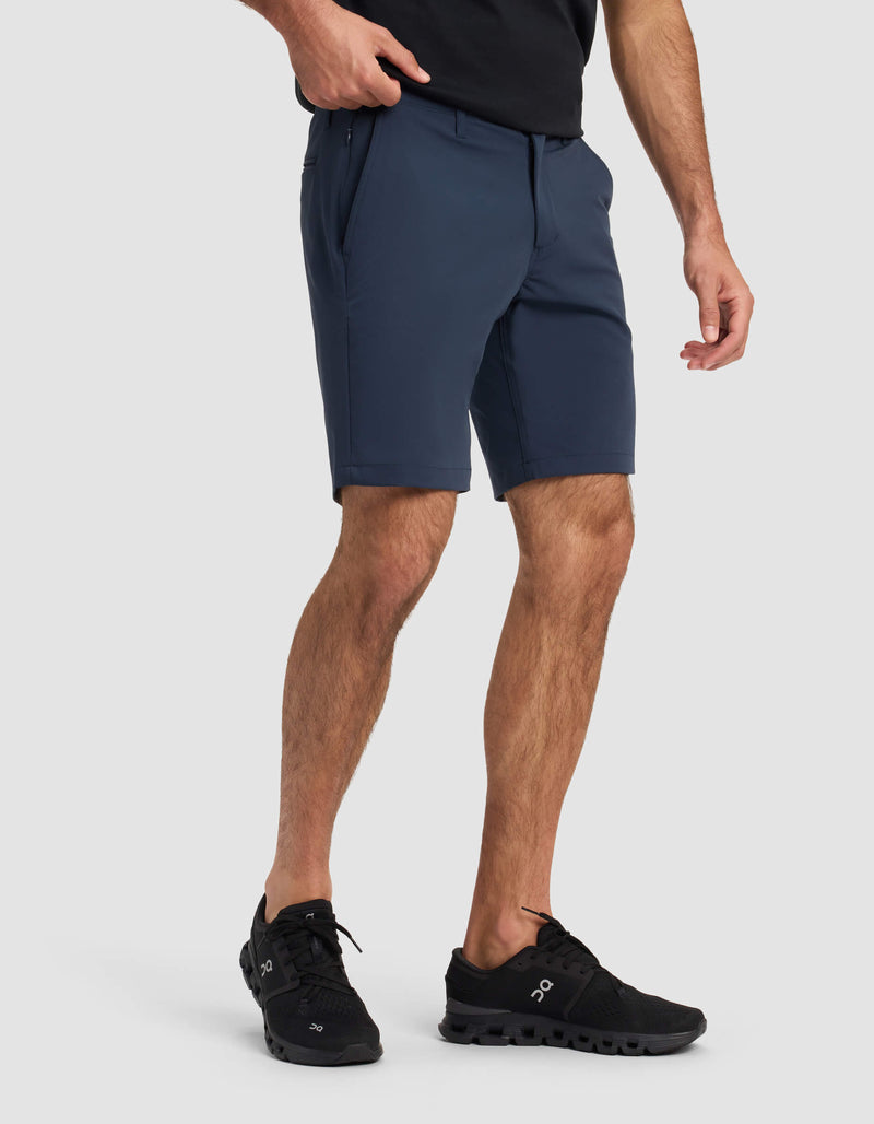 A person wearing a black t-shirt, Cozy Earth Men's Everywhere Short in navy, and black athletic shoes stands against a light gray background with one hand in their pocket.