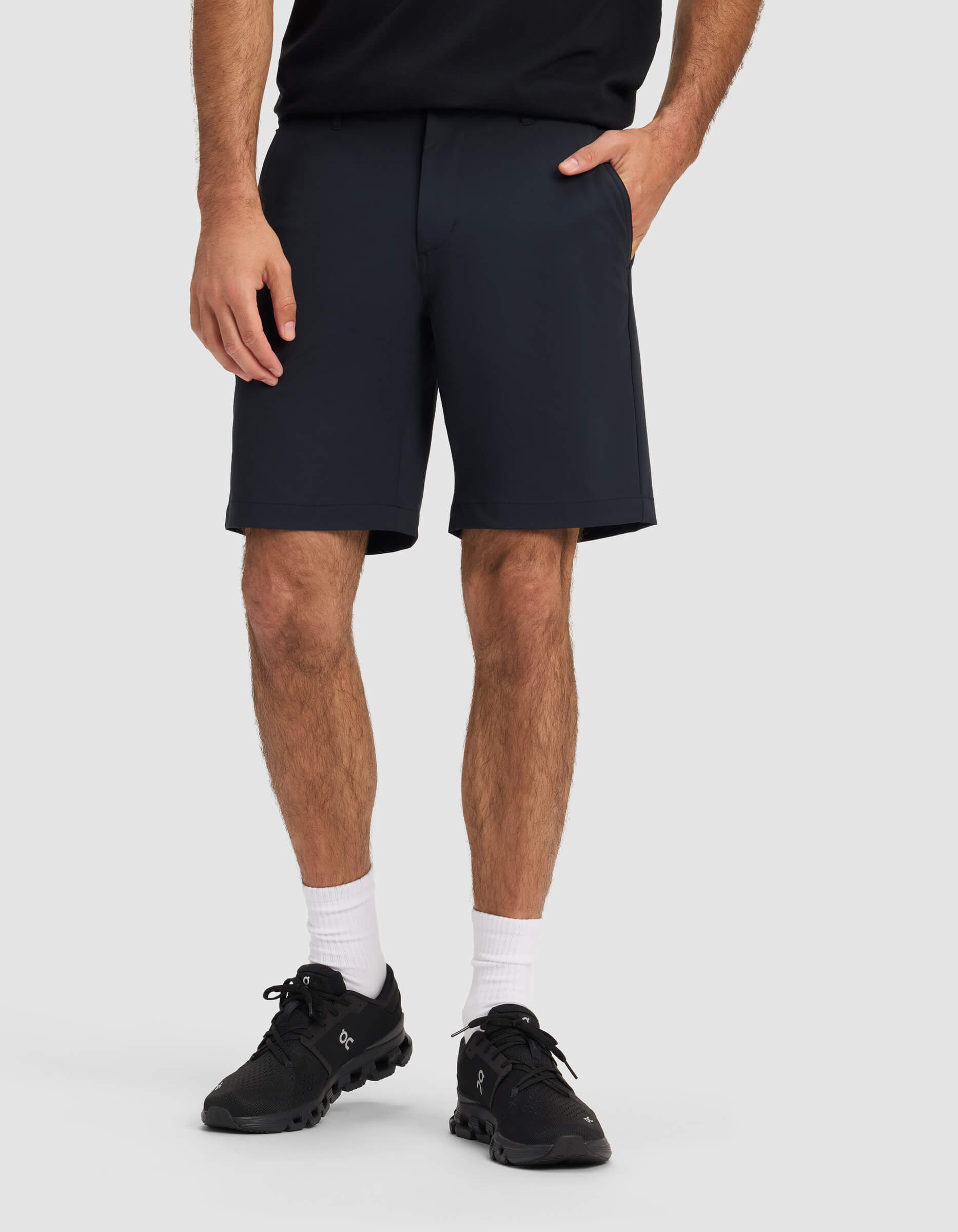 A man wearing Cozy Earth's Men's Everywhere Short in black, a black shirt, black sneakers, and white crew socks stands with one hand in his pocket against a plain light gray background.|Color:Jet Black