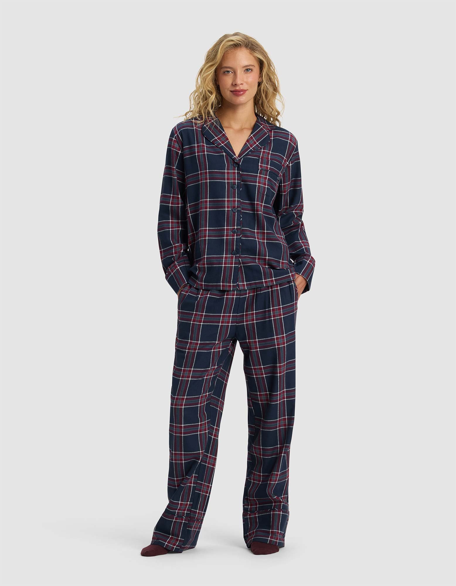 A woman with blonde hair smiles slightly while wearing Cozy Earth’s Women’s Farmhouse Long Sleeve Pajama Set—loose-fitting navy blue pajamas with a red and white plaid pattern, featuring a button-up shirt and matching pants.|Color:Eclipse Plaid