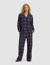A woman with blonde hair smiles slightly while wearing Cozy Earth’s Women’s Farmhouse Long Sleeve Pajama Set—loose-fitting navy blue pajamas with a red and white plaid pattern, featuring a button-up shirt and matching pants.|Color:Eclipse Plaid