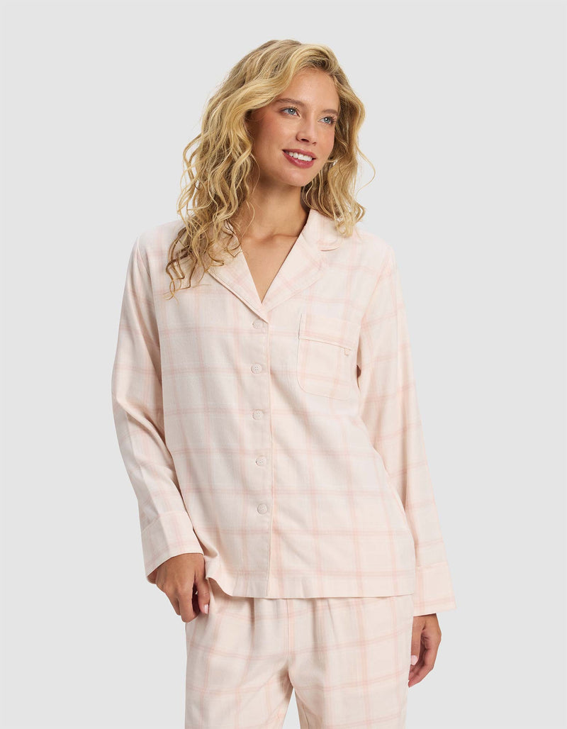A woman with wavy blonde hair models the Cozy Earth Women's Farmhouse Long Sleeve Pajama Top, featuring a light pink plaid design, button-up front, and matching pants, standing against a plain light background and smiling slightly.