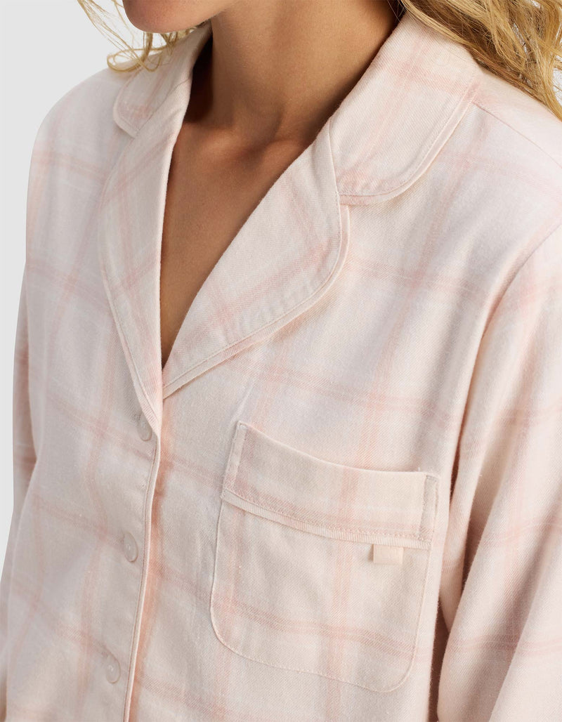 A close-up of a person wearing the Cozy Earth Women's Farmhouse Long Sleeve Pajama Top in pink and white plaid, featuring a chest pocket and buttons, with the upper torso and part of the face visible.