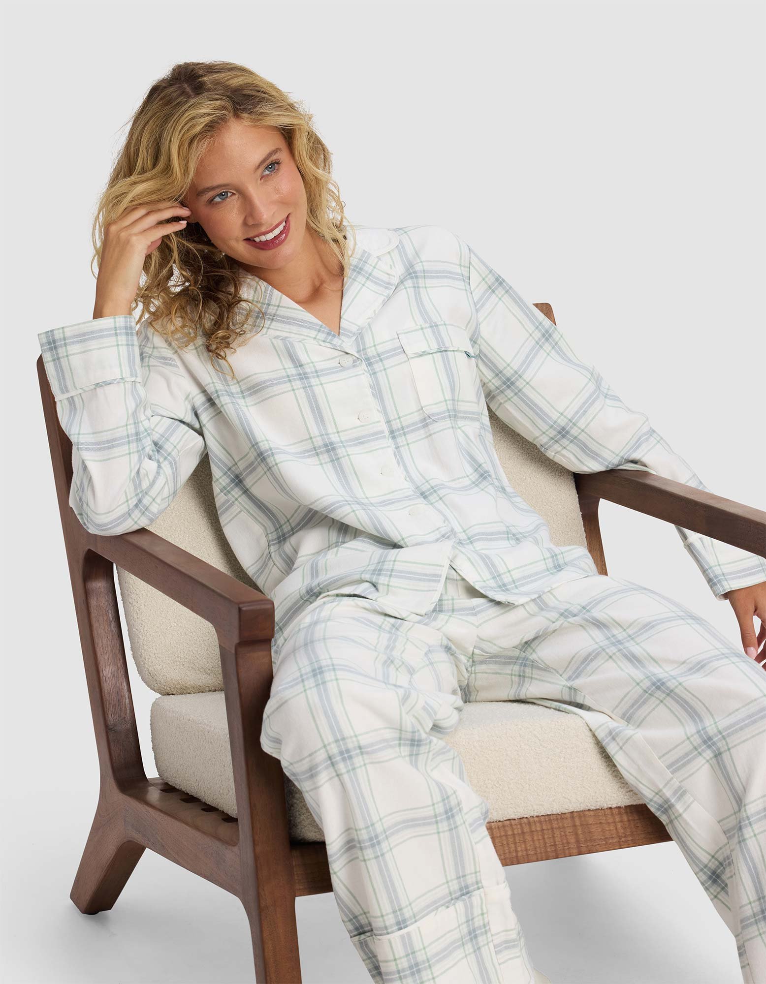A woman with curly blonde hair wears the Cozy Earth Women's Farmhouse Long Sleeve Pajama Top and sits smiling on a cushioned wooden chair against a plain light background.