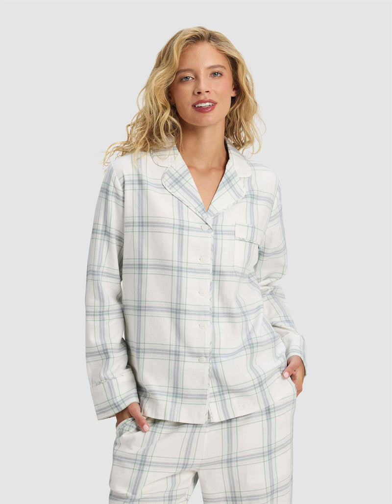 A woman with wavy blonde hair wears the Cozy Earth Women's Farmhouse Long Sleeve Pajama Top and matching pants, standing with her hands in her pockets against a plain, light background.