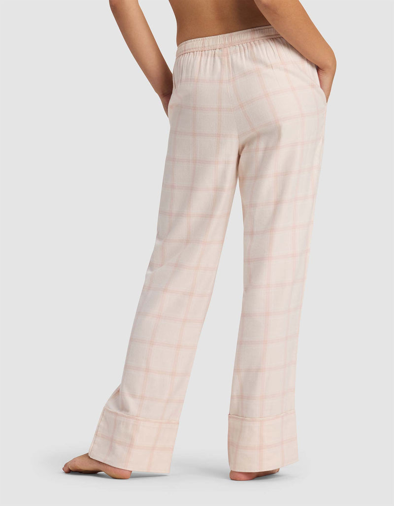 A woman is seen from behind wearing Cozy Earth's Women's Farmhouse Pajama Pant in light pink plaid with an elastic waistband, standing barefoot against a light background.