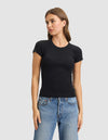 A woman wearing the Cozy Earth Women's Fine Ribbed Tee in black and blue jeans stands against a light gray background, looking to her left with one hand relaxed by her side. |Color:Jet Black