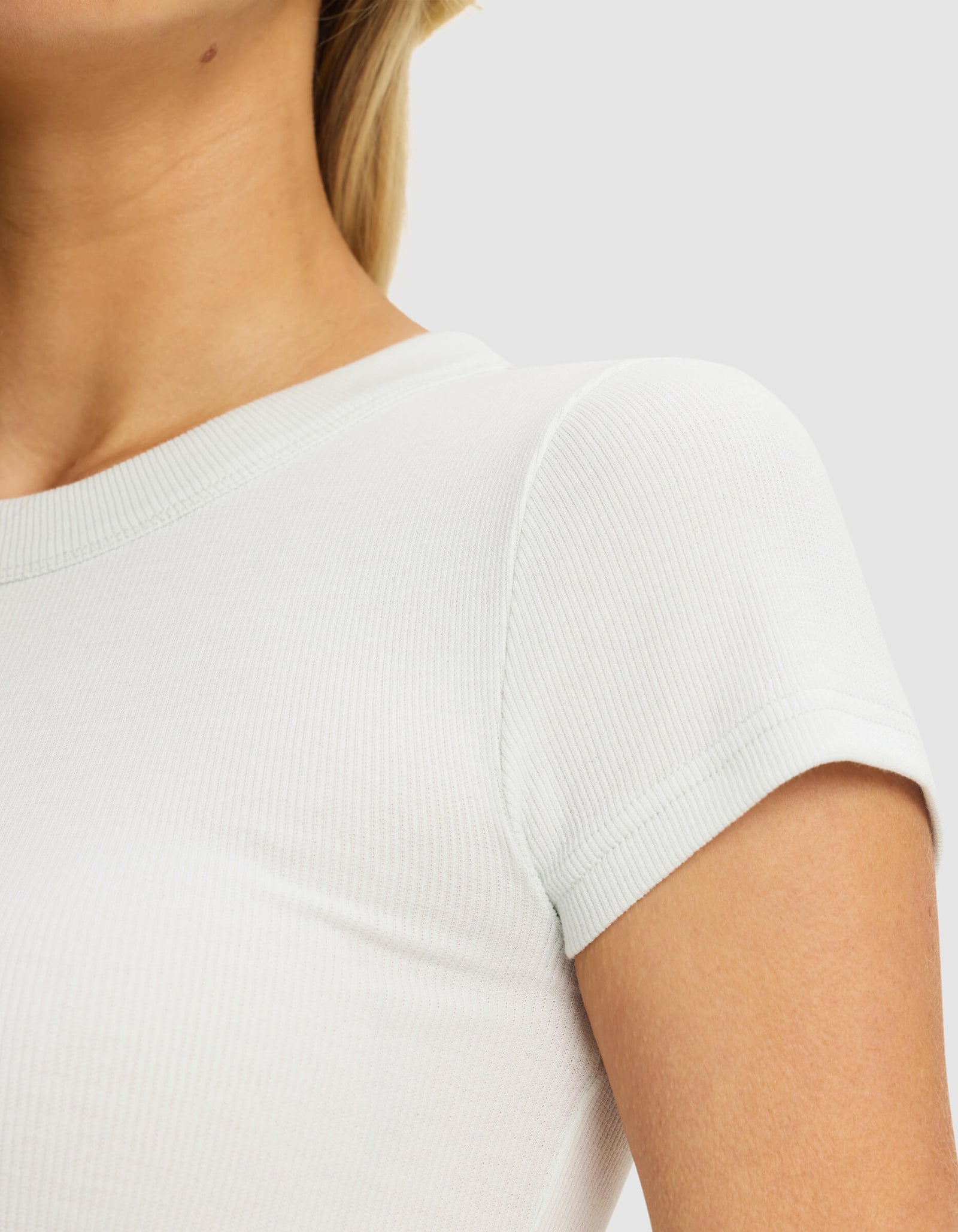 Close-up of a woman wearing the Cozy Earth Women's Fine Ribbed Tee in white, highlighting the ribbed texture, short sleeves, and upper torso against a plain light background.