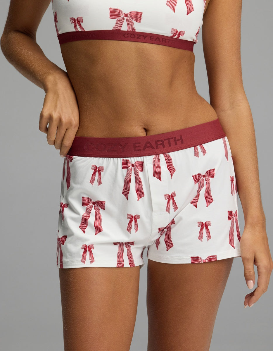 A person wearing Cozy Earth Women’s First Layer Pajama Boxer Short in white with a red bow print and a maroon elastic waistband.