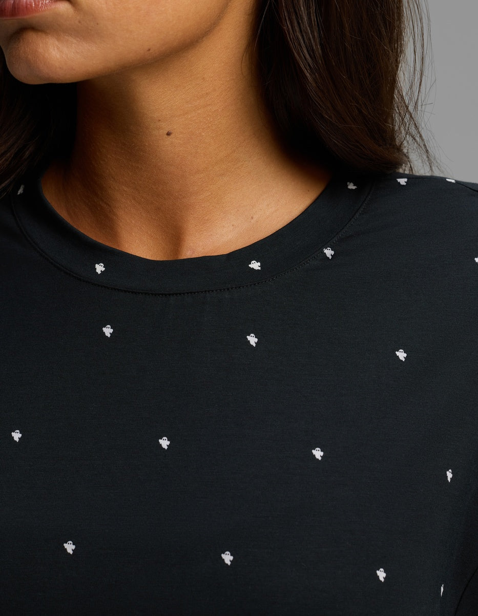 Close-up of a woman wearing the Cozy Earth Women’s First Layer Boyfriend Sleep Tee in black with small white polka dot patterns. The image highlights her neck, part of her face, and the upper portion of the shirt.