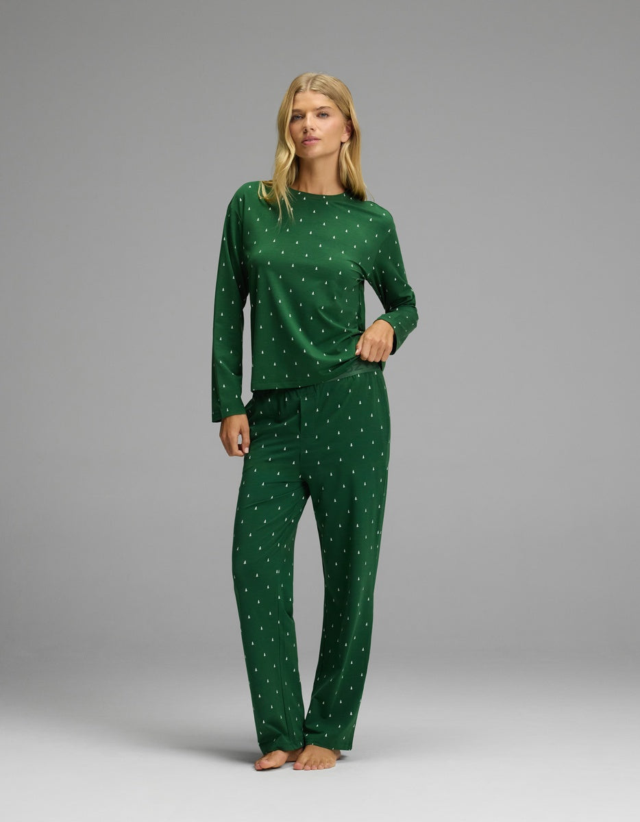 A person wearing a forest green Women’s First Layer Long Sleeve Sleep Tee & Pajama Pant Set by Cozy Earth, featuring a small white tree pattern on the long-sleeved top and matching straight-leg pants.