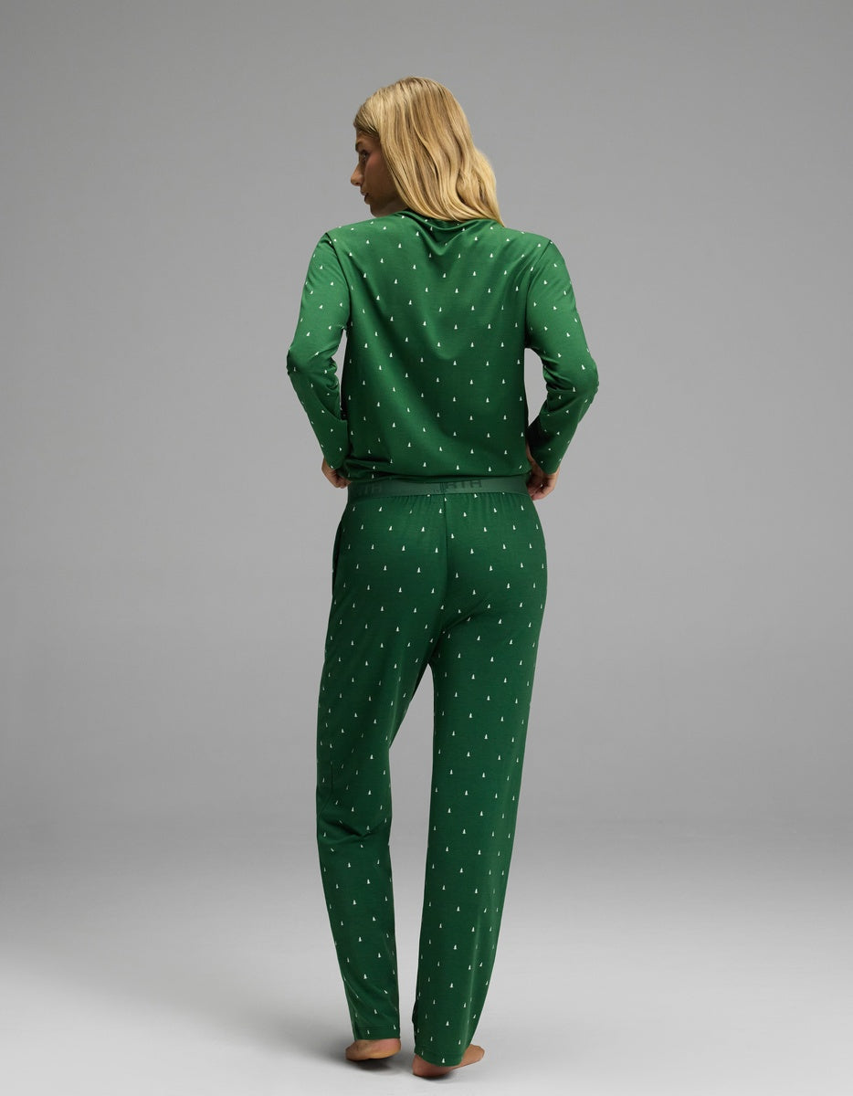A woman wearing a green Cozy Earth Women’s First Layer Long Sleeve Sleep Tee & Pajama Pant Set featuring a white tree print.