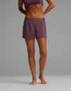 A person standing barefoot against a plain gray background, wearing Cozy Earth’s Women’s First Layer Pajama Boxer Short in mauve with a matching sports bra. Only the body from shoulders to feet is visible.|Color:Fig