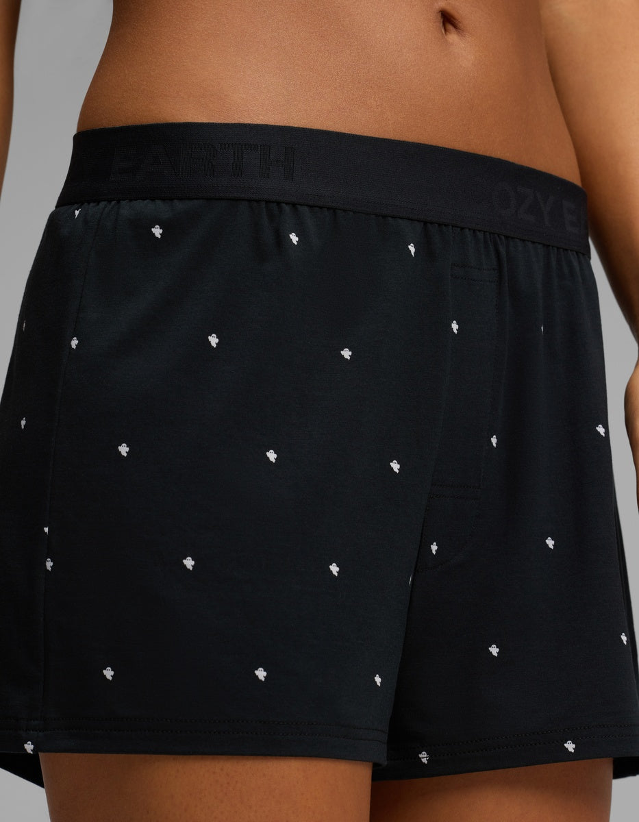 Close-up of a person wearing Cozy Earth Women’s First Layer Pajama Boxer Shorts in black with a small white dot pattern. The waistband is black with subtle text branding, and the background is plain gray.