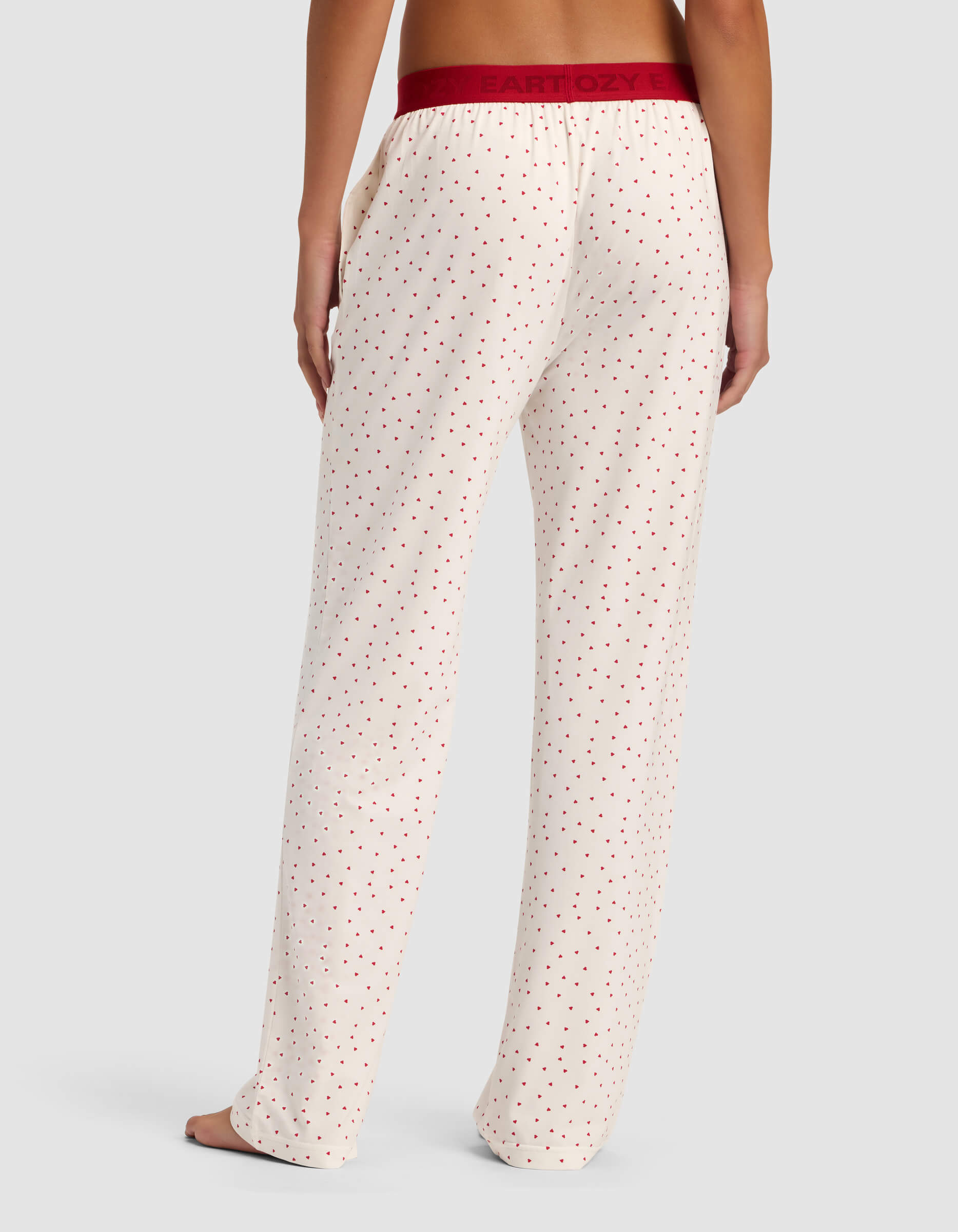 A person stands barefoot, facing away, wearing Cozy Earth Women's First Layer Pajama Pant in cream with small red polka dots and a burgundy waistband against a plain light background.