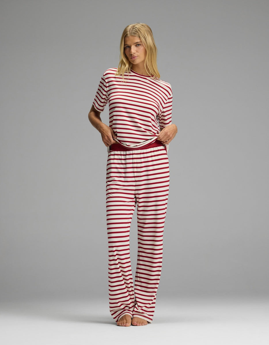 A woman wearing a Cozy Earth Women’s First Layer Pajama Pant and matching short-sleeved top, both featuring a red-and-white horizontal stripe pattern.