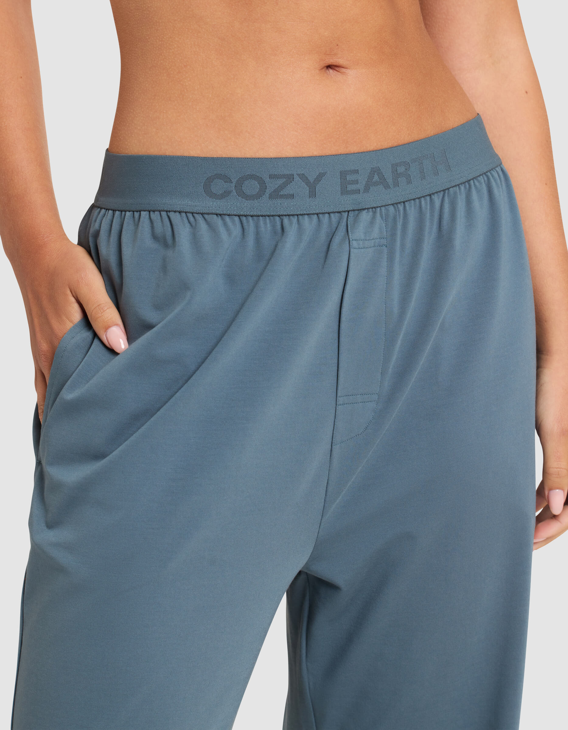 Close-up of a person wearing Cozy Earth Women's First Layer Pajama Pant in blue, with their hand in the pocket and "COZY EARTH" on the waistband, highlighting the fit and soft fabric texture.