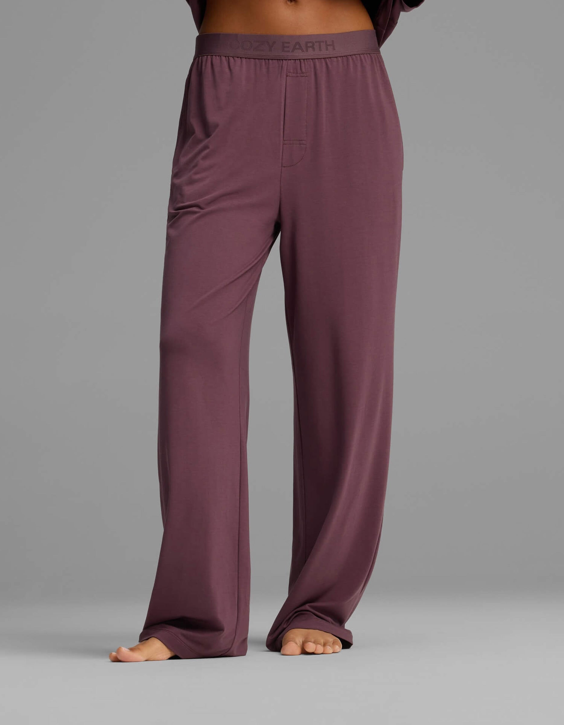 A person is barefoot against a plain gray background, wearing Cozy Earth’s Women’s First Layer Pajama Short Sleeve Tee & Pant Set, featuring loose-fitting, high-waisted mauve pants with an elastic waistband.