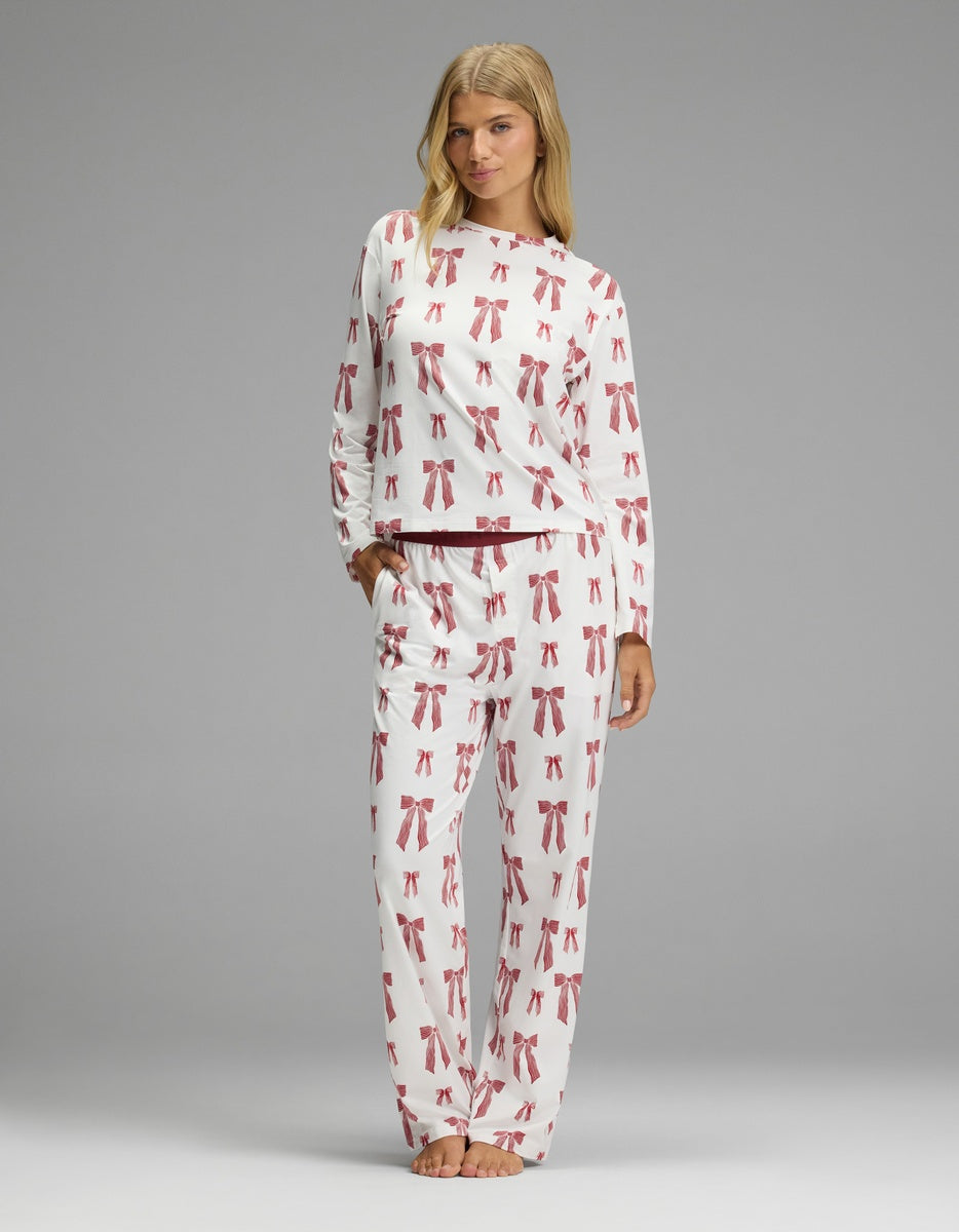 A woman wearing a white long-sleeved shirt and matching Women’s First Layer Pajama Pant, both featuring an all-over print of red bows.