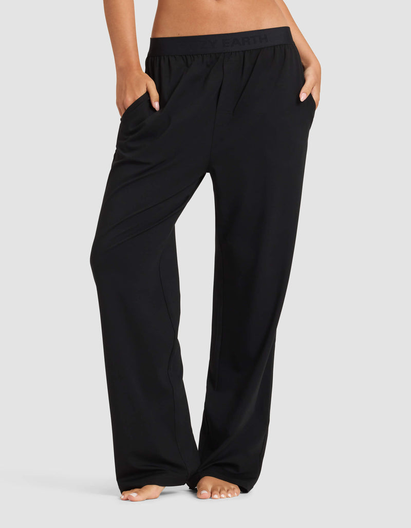 A person stands barefoot against a plain light background, wearing Cozy Earth’s Women's First Layer Pajama Pant in black, showcasing the relaxed fit and waistband with hands in pockets.