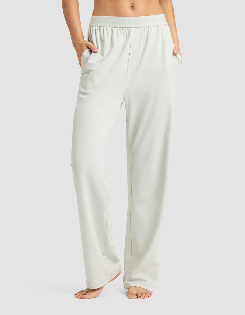 A person stands barefoot with hands in pockets, wearing Cozy Earth Women's First Layer Pajama Pant—light-colored, loose-fitting lounge pants featuring a relaxed fit and elastic waistband. Upper body is not visible.