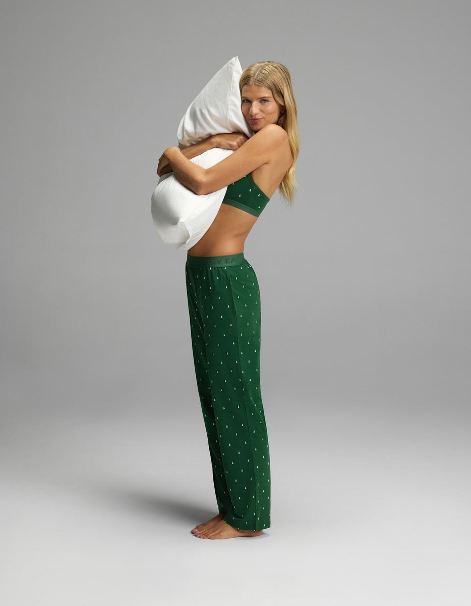 A woman wearing Women’s First Layer Pajama Pant in green with a small white print and a matching bralette, hugging a white pillow.