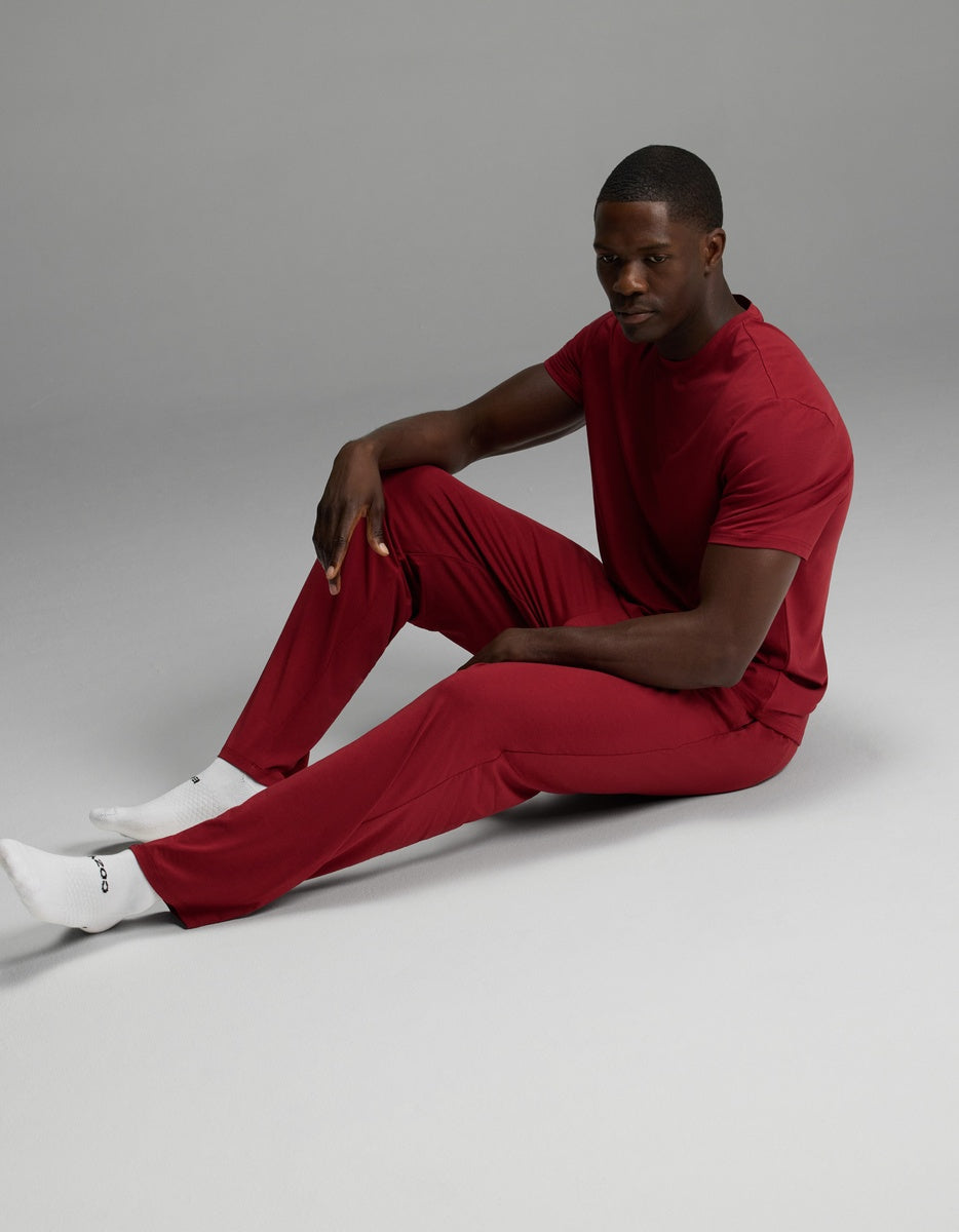 A man sitting on the floor wearing a matching dark red short-sleeved t-shirt and Cozy Earth Men’s First Layer Pajama Pant with white socks.