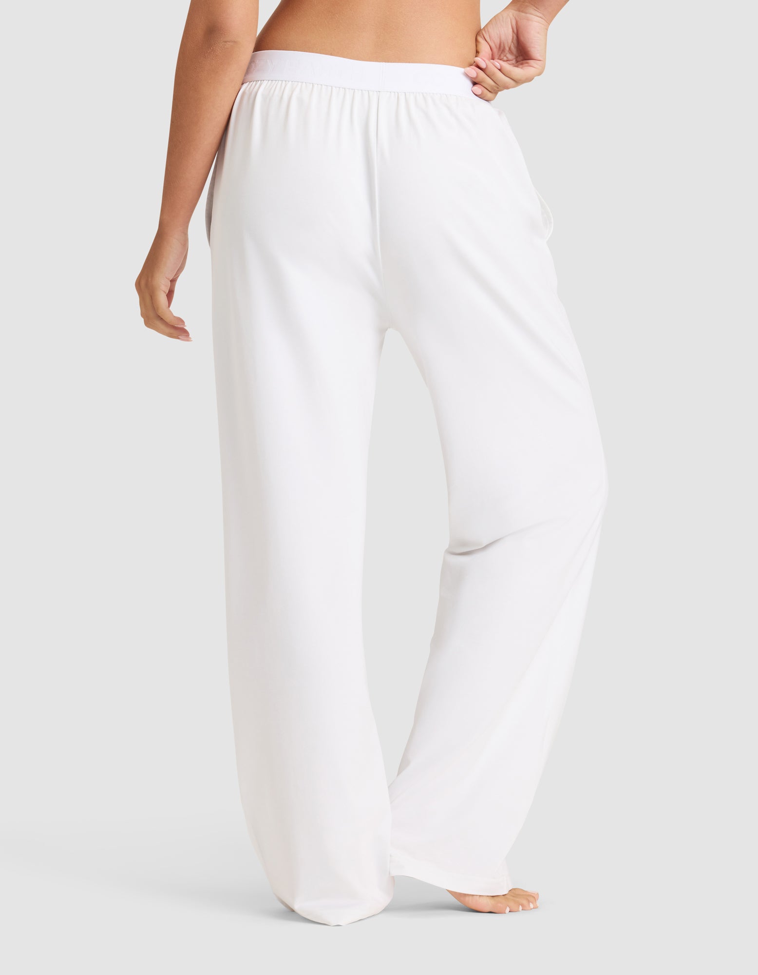 A person wearing Cozy Earth's Women's First Layer Pajama Pant is barefoot on a light gray background, shown from the waist down and viewed from the back.