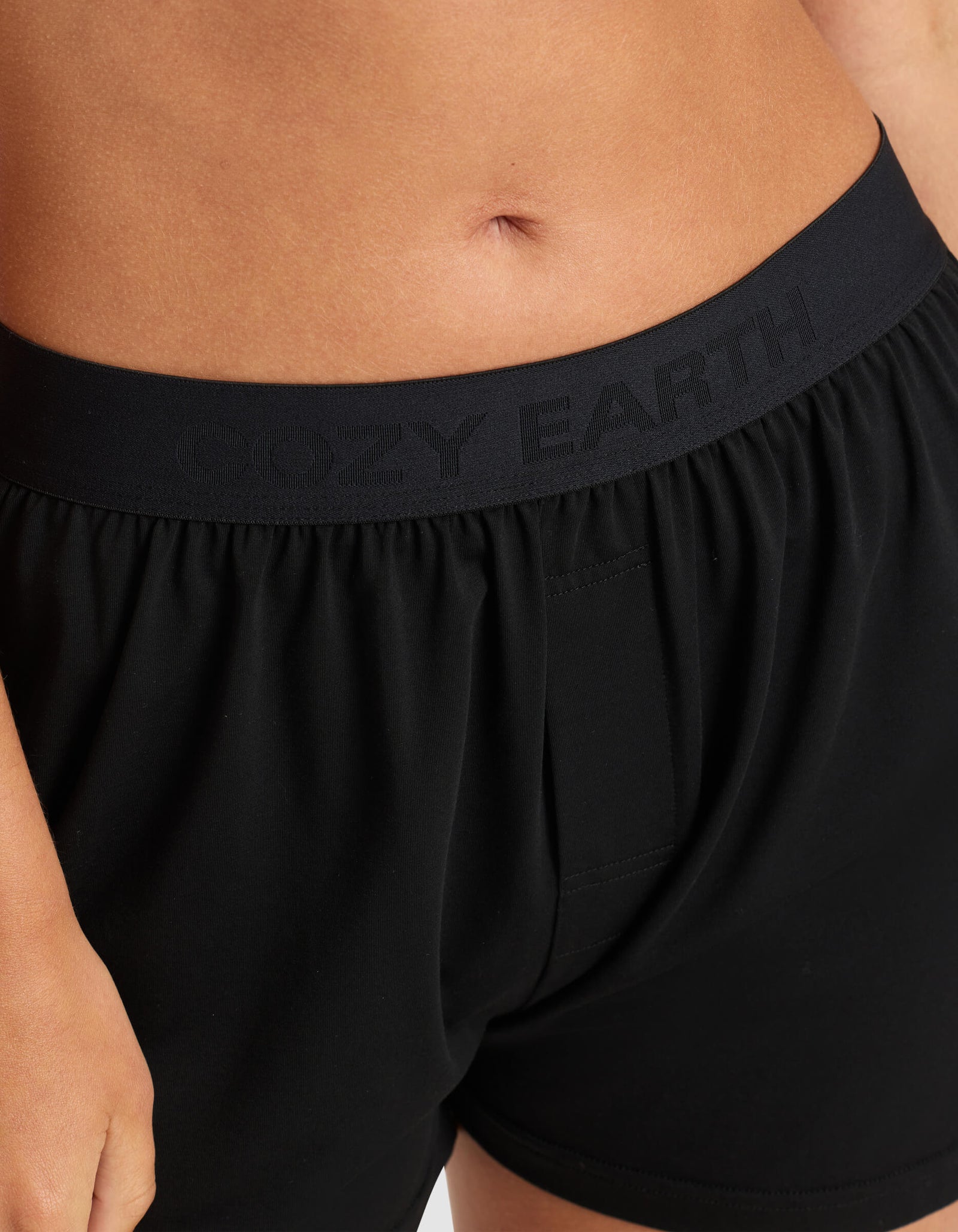 Close-up of a person wearing Cozy Earth Women's First Layer Pajama Short Sleeve Tee & Boxer Short Set, featuring black boxer shorts with a waistband embossed with “COZY EARTH.” Only the lower torso and upper thighs are visible.