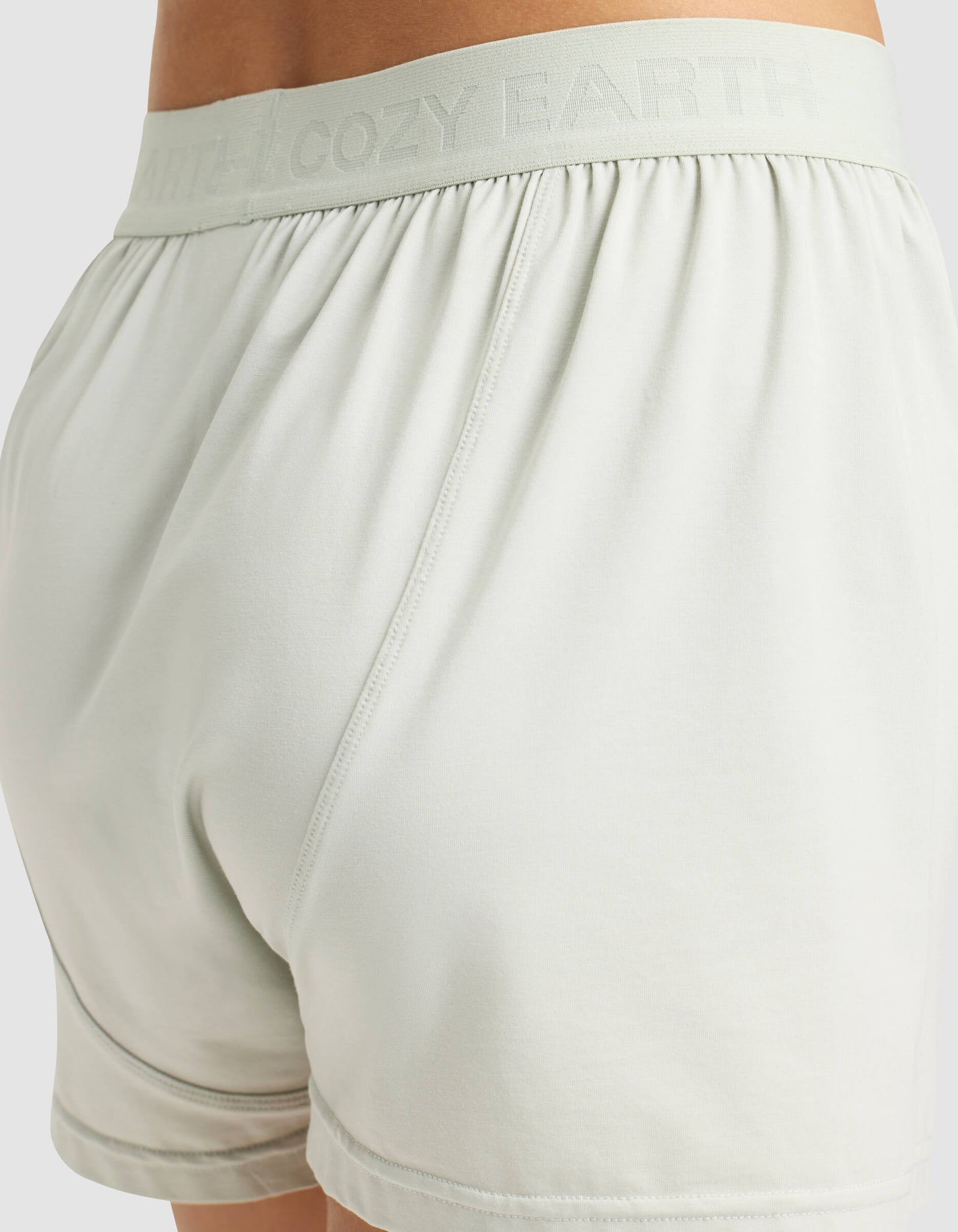 Close-up of a person wearing Cozy Earth Women's First Layer Pajama Short Sleeve Tee & Boxer Short Set in light-colored shorts with a soft, smooth fabric and an elastic waistband subtly embossed with the Cozy Earth logo.