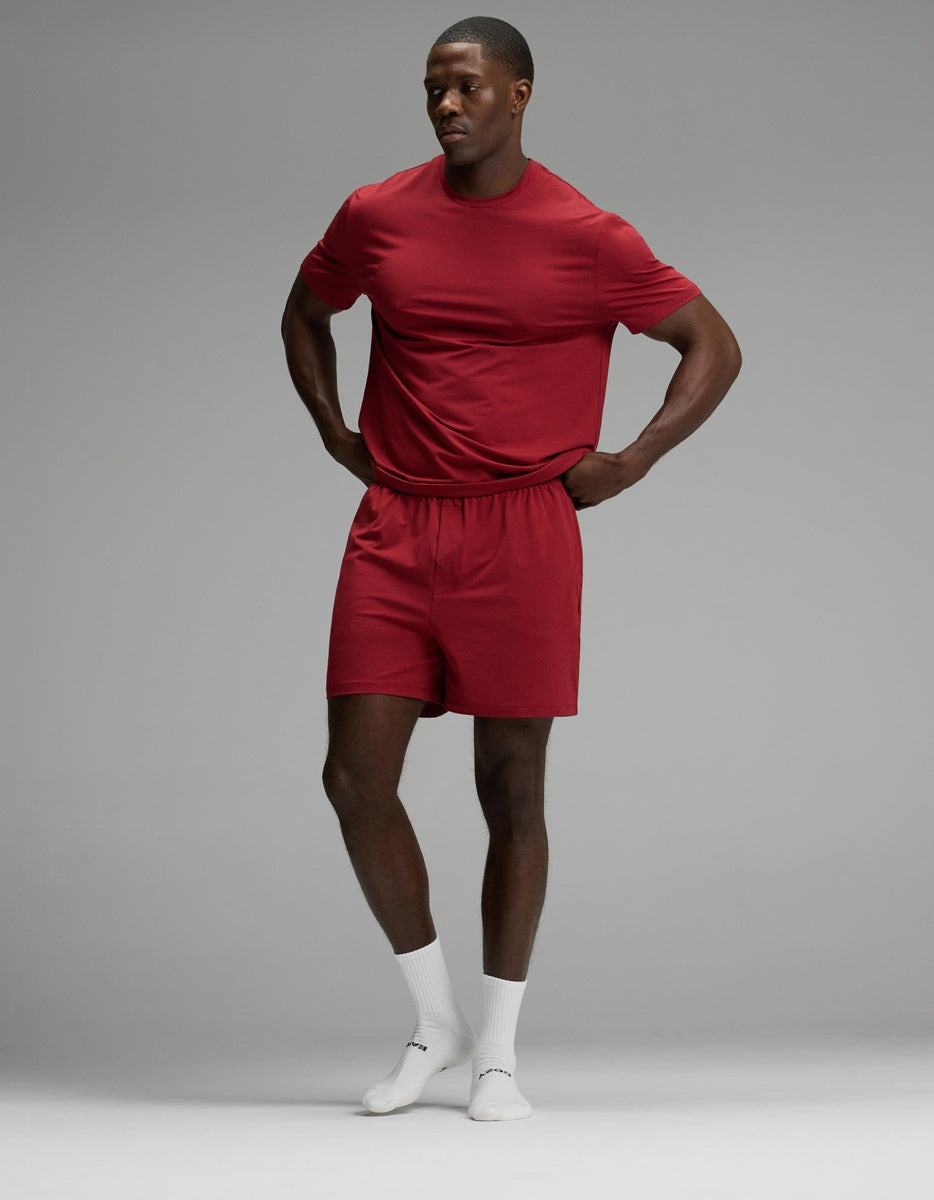 A man wearing a matching red Cozy Earth Men’s First Layer Pajama Short set, consisting of a short-sleeve t-shirt and pajama shorts, paired with white crew socks.