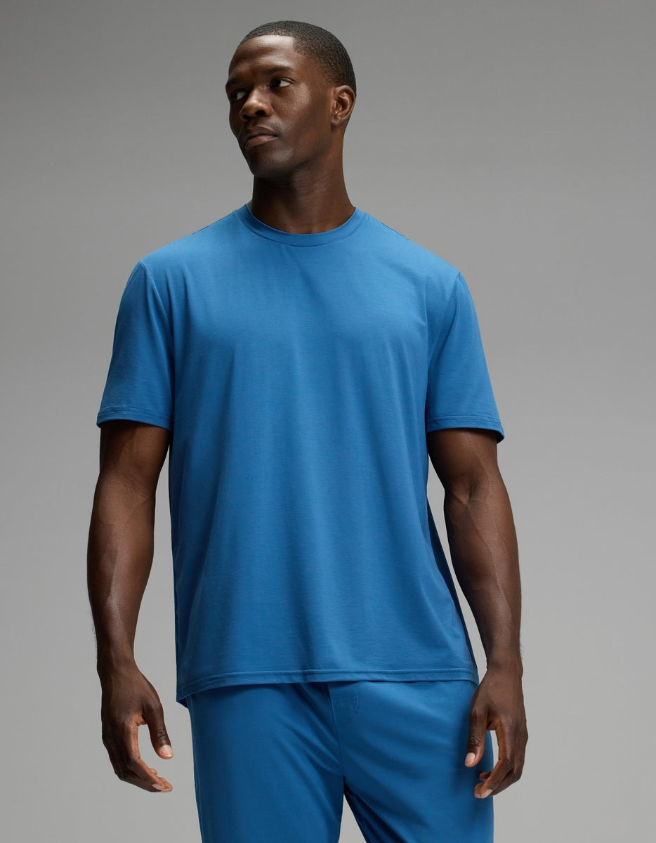 A man wearing the Cozy Earth Men’s First Layer Pajama Short Sleeve Tee in blue and matching blue pants stands against a plain gray background, looking slightly to his left with a neutral expression.|Color:Anchor