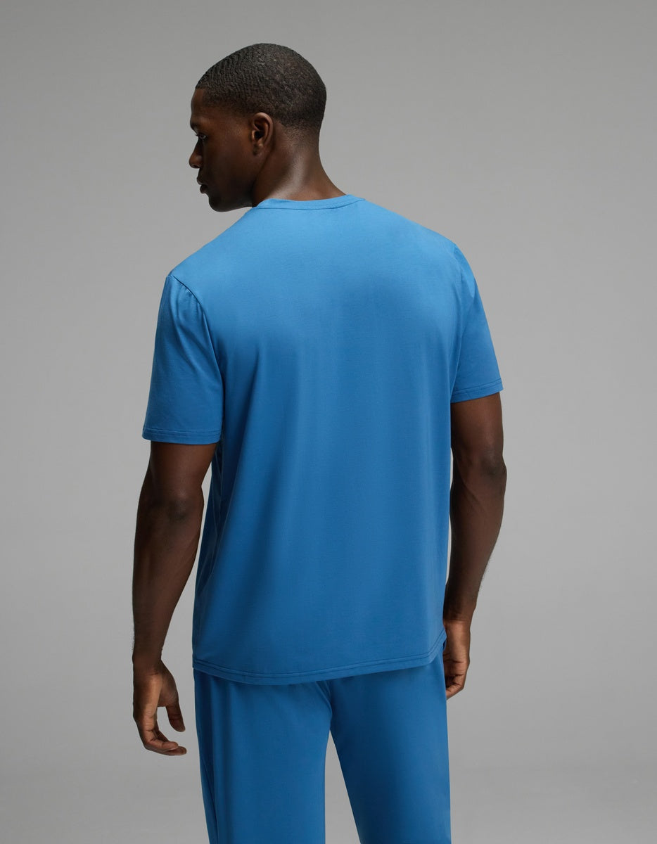 A man stands facing away, wearing the Cozy Earth Men’s First Layer Pajama Short Sleeve Tee and matching pants, against a plain gray background.