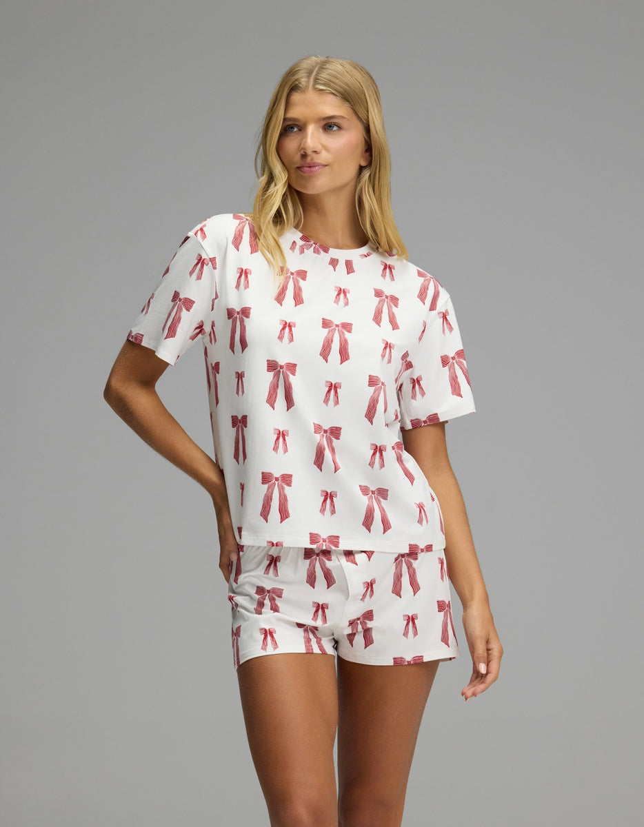 A woman wears a white Cozy Earth Women’s First Layer Pajama Short Sleeve Tee & Boxer Short Set featuring a print of small red bows.