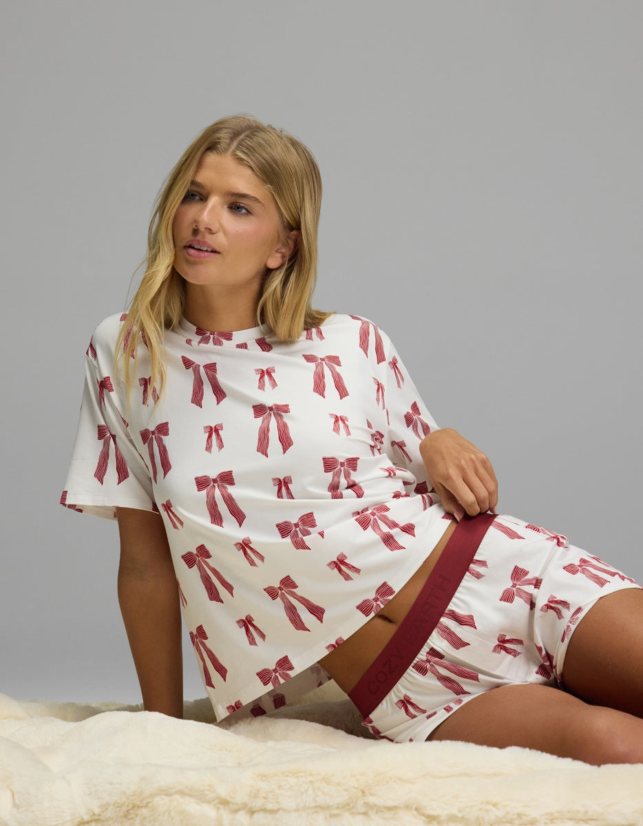 A woman wearing a Cozy Earth Women’s First Layer Pajama Short Sleeve Tee & Boxer Short Set in white with a red bow pattern.