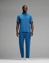 A man stands against a gray background wearing the Cozy Earth Men’s First Layer Pajama Short Sleeve Tee & Pant Set in blue with white socks, looking slightly to the side.|Color:Anchor
