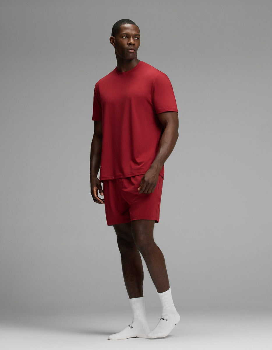 A man wears a red short-sleeve Men’s First Layer Pajama Short Sleeve Tee & Short Set with matching red shorts and white socks.