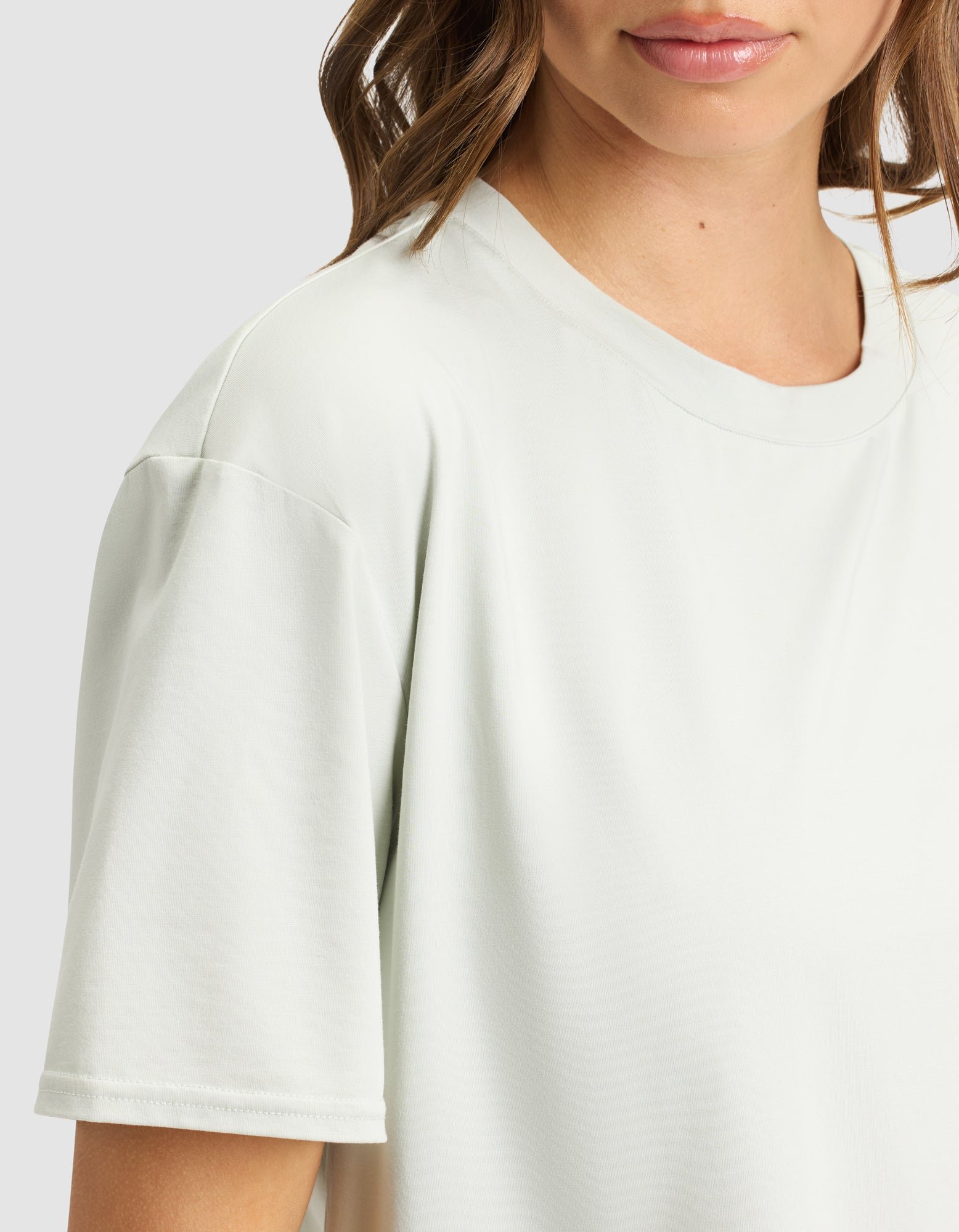 A woman wears the Cozy Earth Women's First Layer Pajama Short Sleeve Tee in a light color. Only her lower face, neck, shoulder, and upper torso are visible against a plain background.