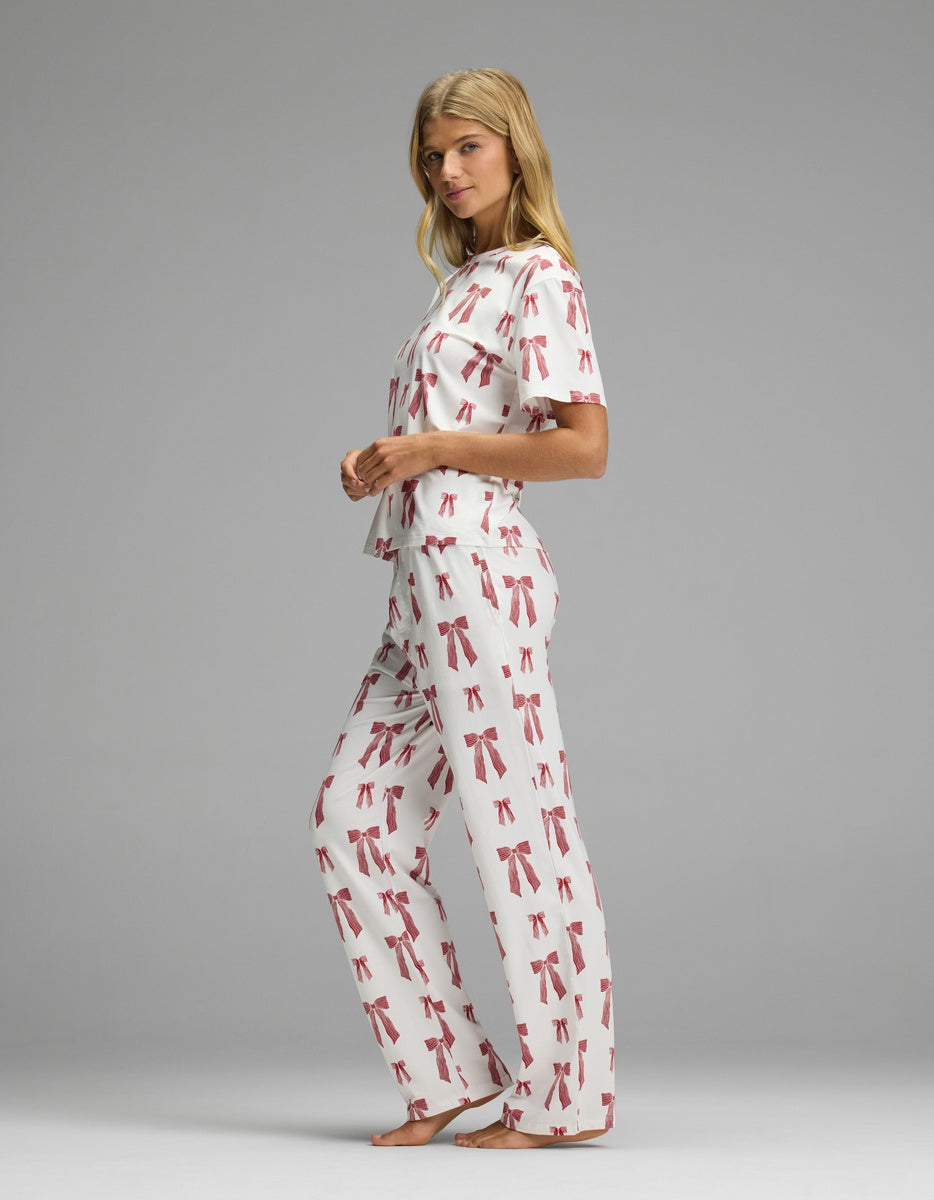 A woman wearing a Cozy Earth Women’s First Layer Pajama Short Sleeve Tee & Pajama Pant Set in a matching red ribbon print.
