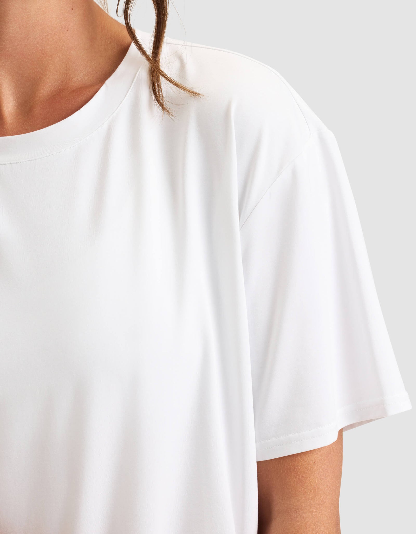 Close-up of a woman wearing the Cozy Earth Women's First Layer Pajama Short Sleeve Tee in white, showing only her neck, shoulder, and arm against a light gray background.
